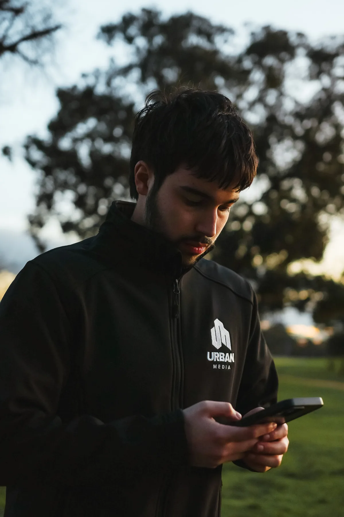 Gabe checking his phone in a park at golden hour