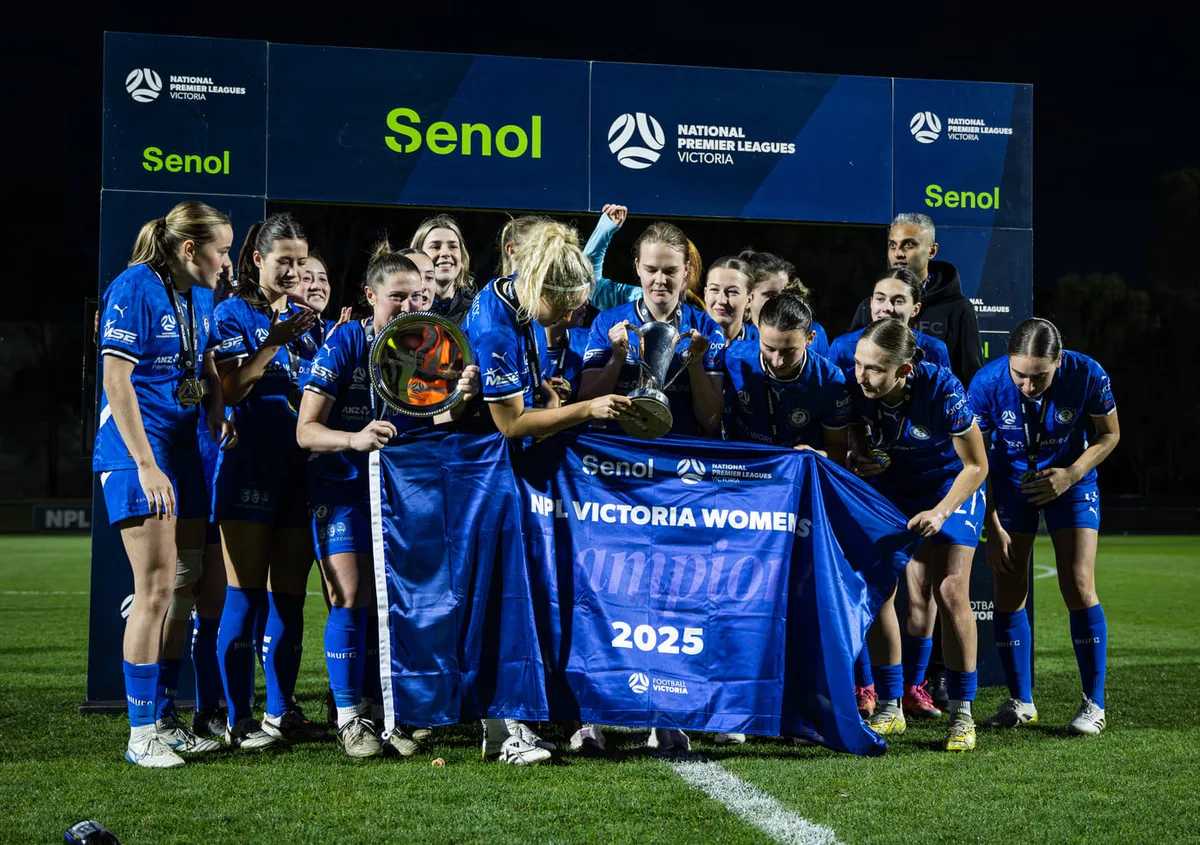 Box Hill United women's team holding the NPL Victoria Women banner on the pitch at night