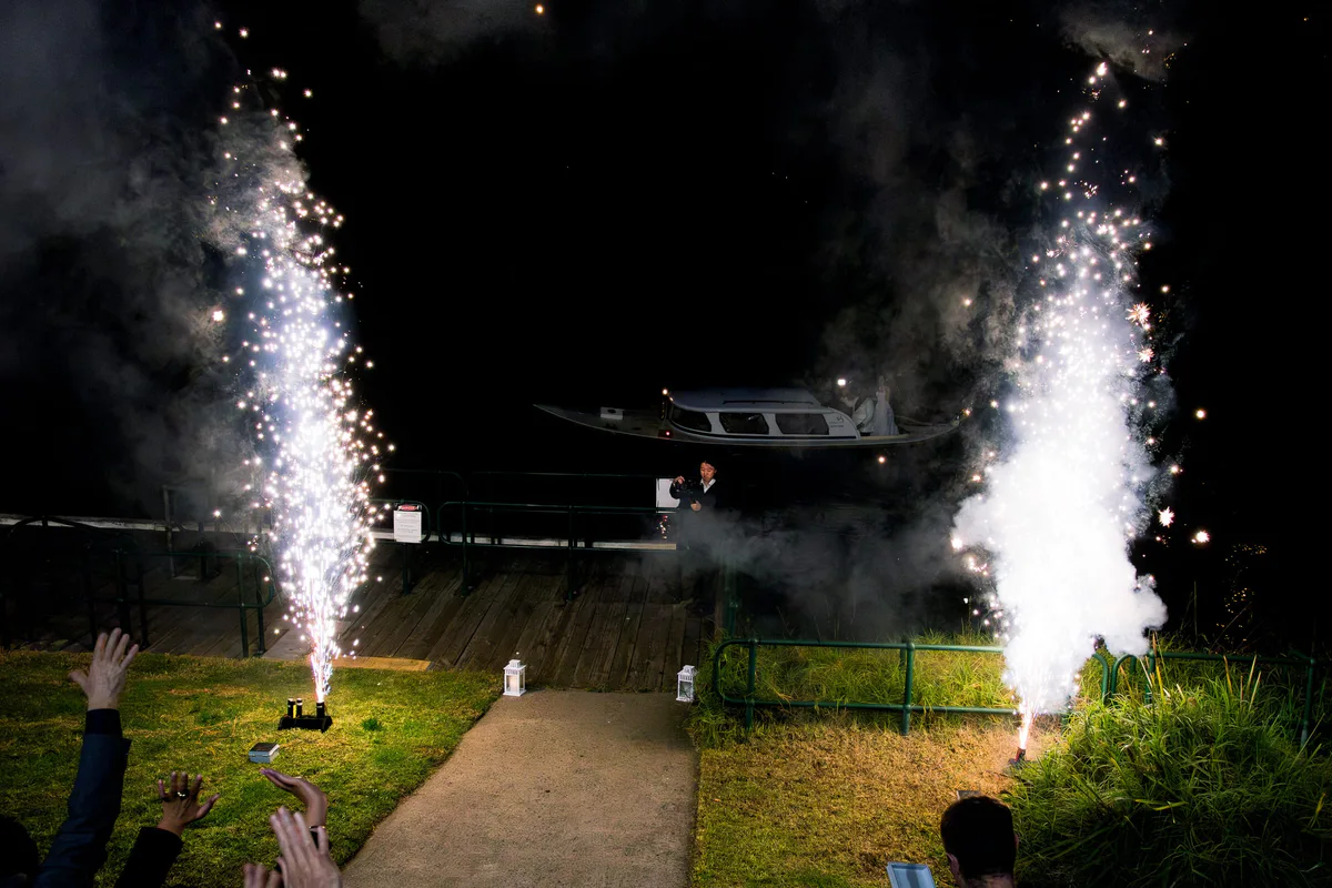 Ground fountains firing beside a jetty as a boat arrives, guests watching