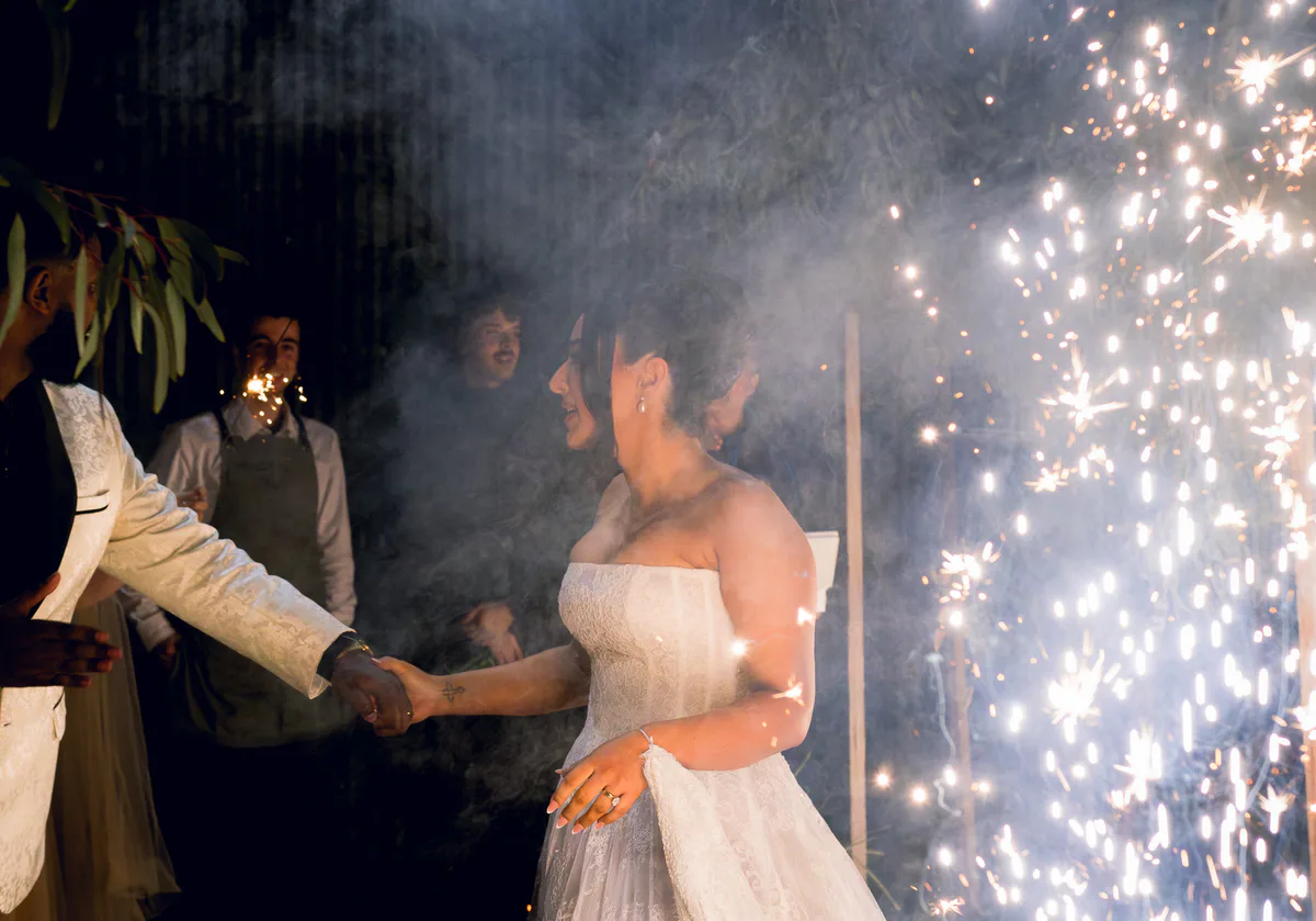 A bride and groom walk out between cold-spark fountains.