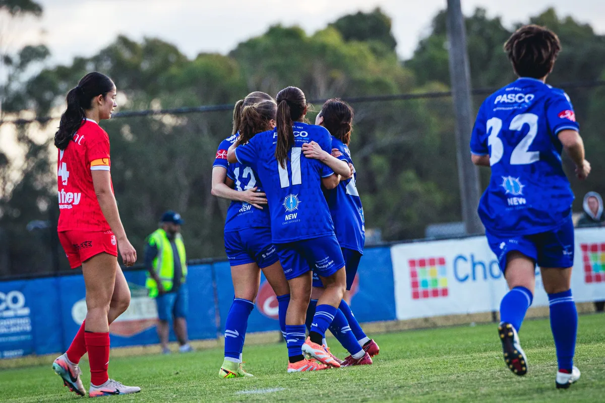 Box Hill United players in blue celebrate as a player in red walks past.