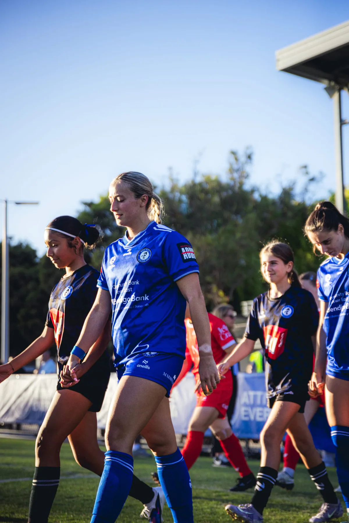 Box Hill United players in blue walk off the pitch, opponents in red behind.