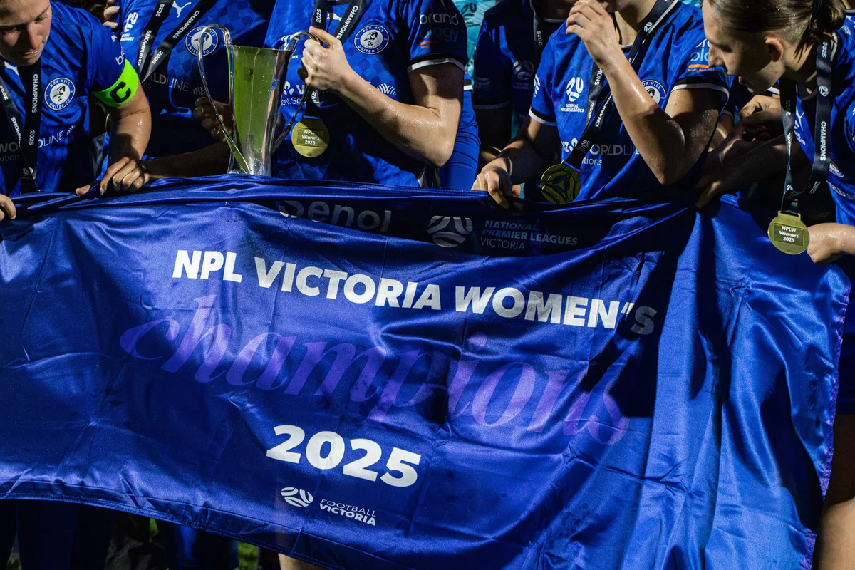 Box Hill United players hold up a blue NPL Victoria Women's 2025 champions banner, cheering.