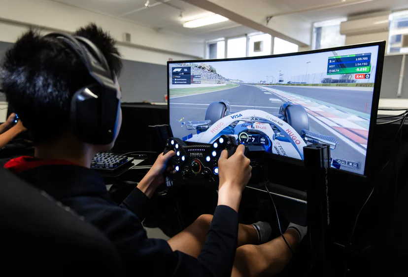 A student in a headset at a racing simulator, a Formula 1 game on the curved screen