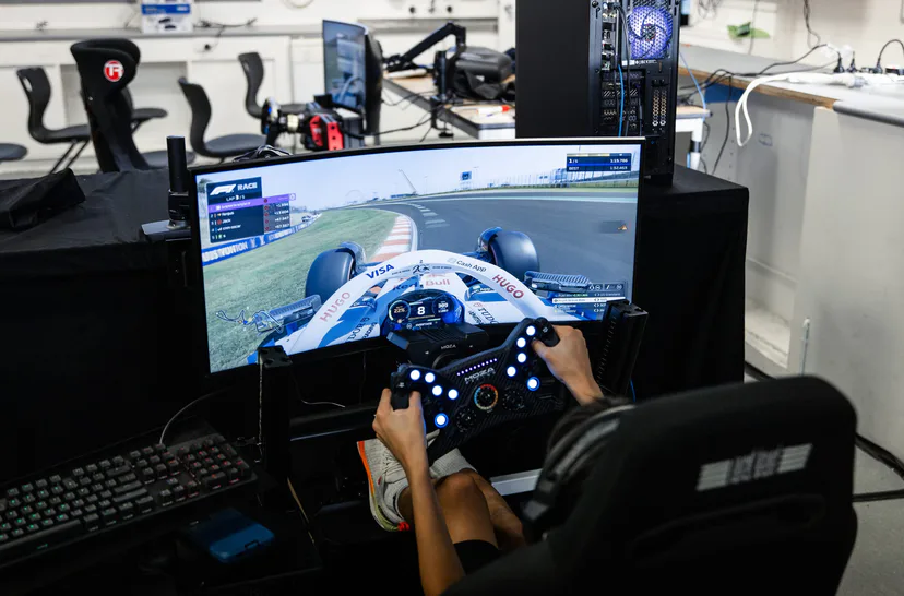 Looking down on hands at a sim racing wheel, a Formula 1 game on the screen