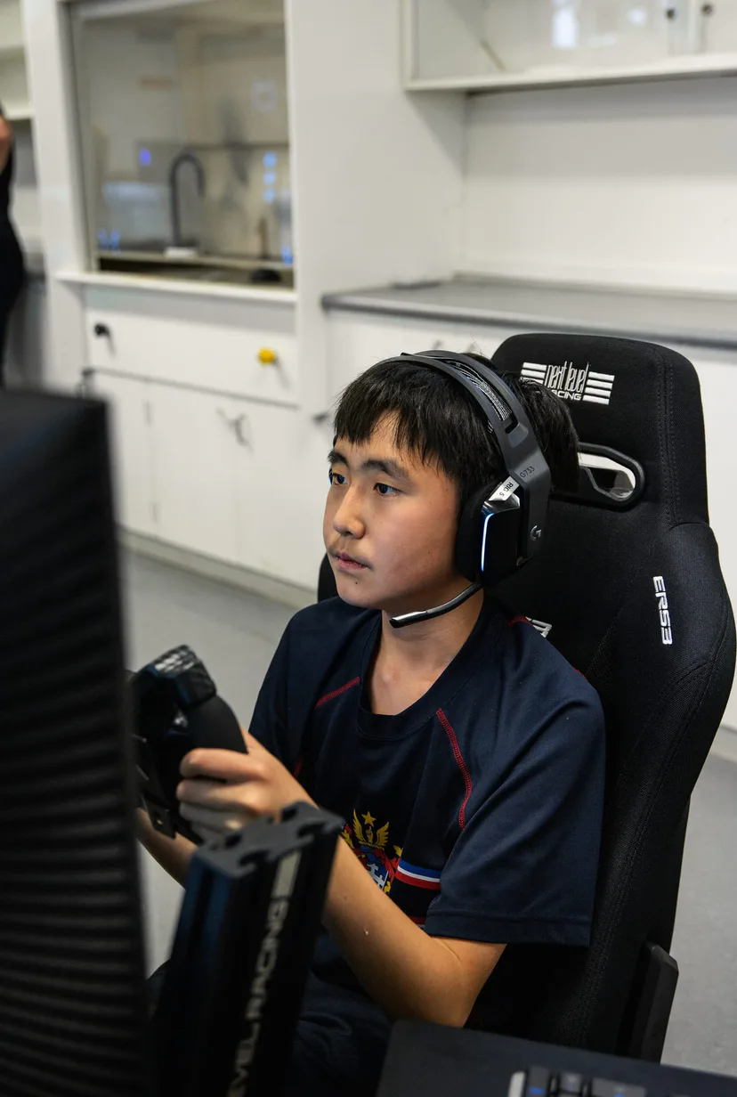 A student in a headset concentrating at a racing simulator, hands on the wheel