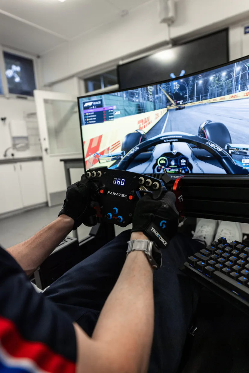 Over the shoulder at a simulator rig, night race on screen and the wheel readout lit