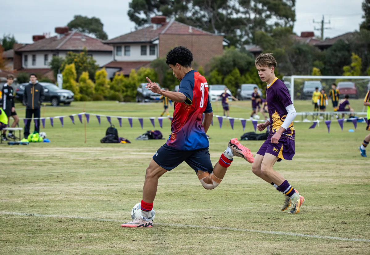 A Brighton Grammar First XI player in red and navy plays the ball in a 2025 match.