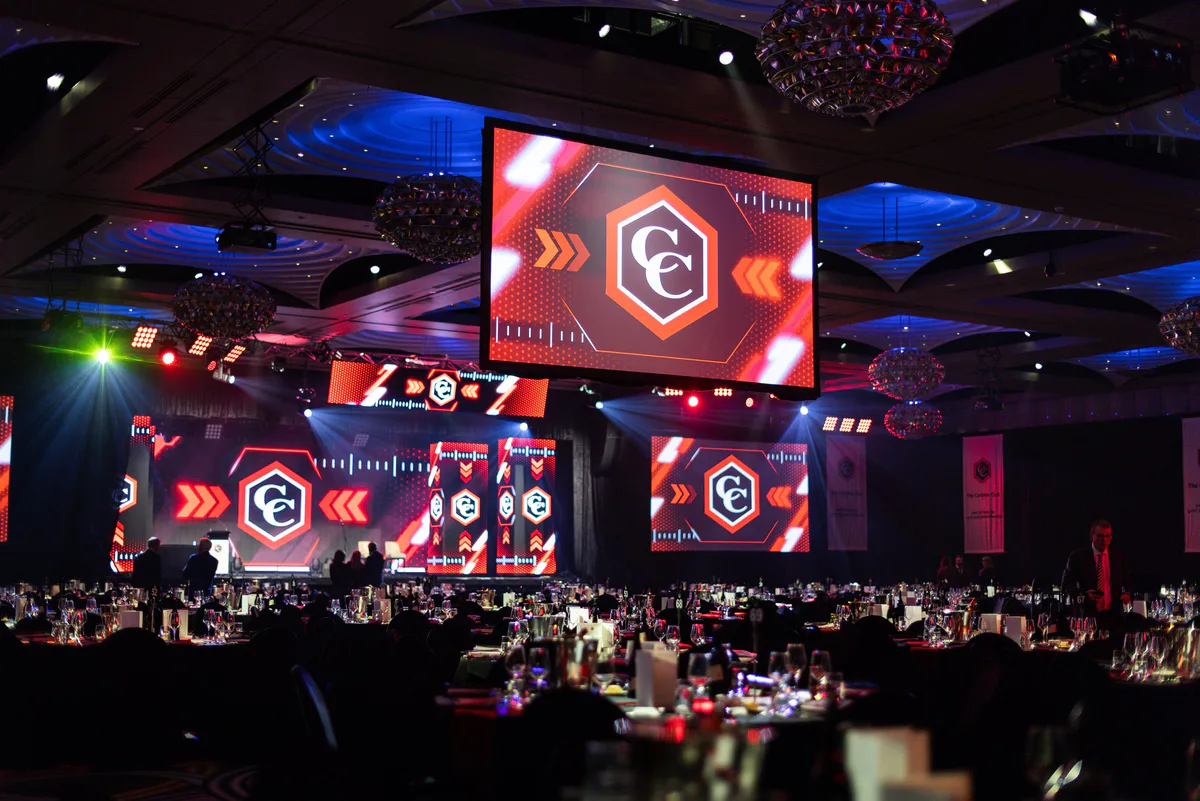 The ballroom stage lit red, Carbine Club marks on the screens