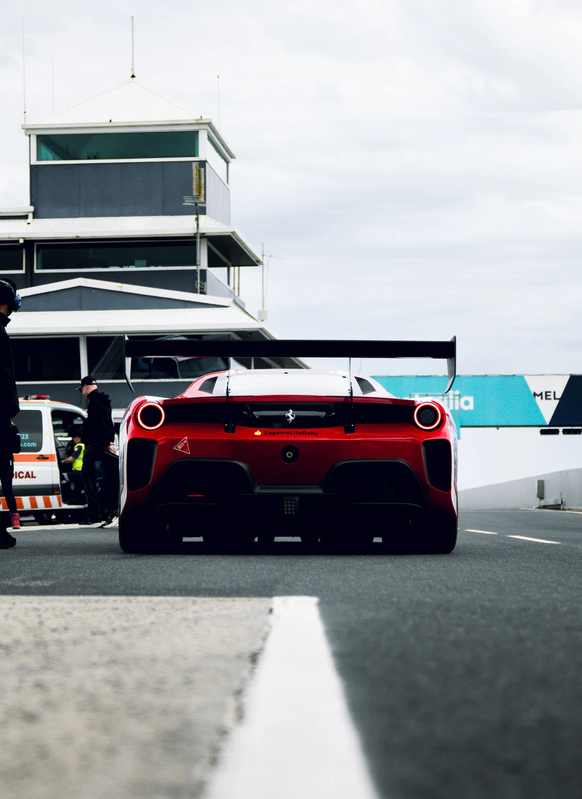 A red Ferrari from behind in pit lane, the control tower above.