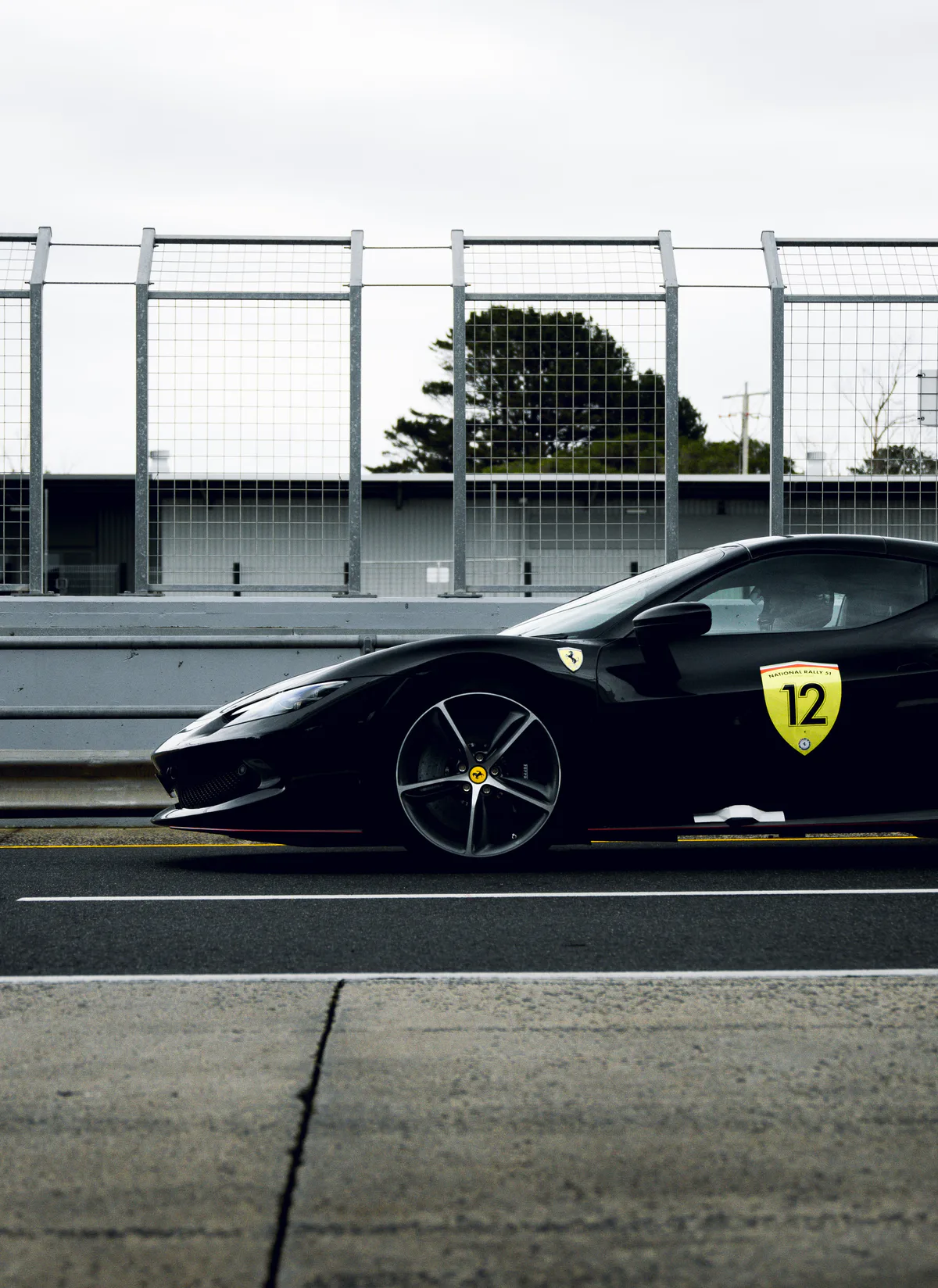 A black Ferrari, number 12, side on against the pit wall.
