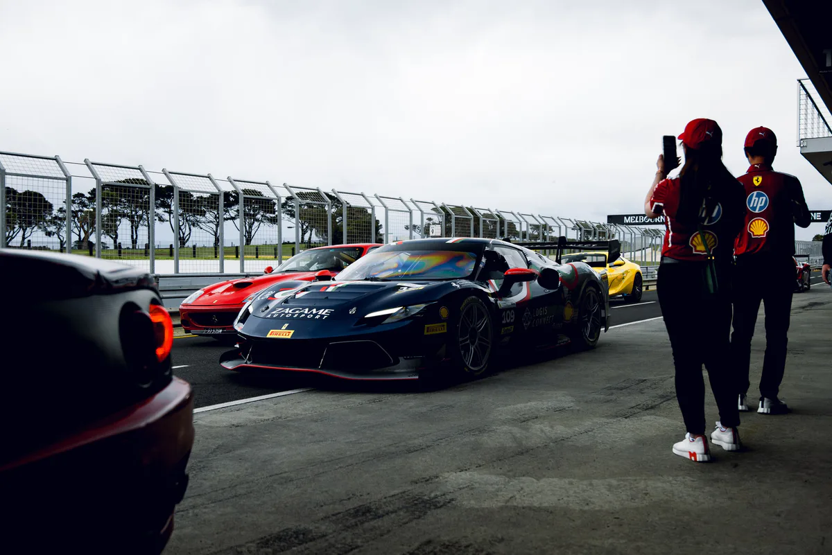 Ferraris queued in pit lane while two people in team gear photograph them