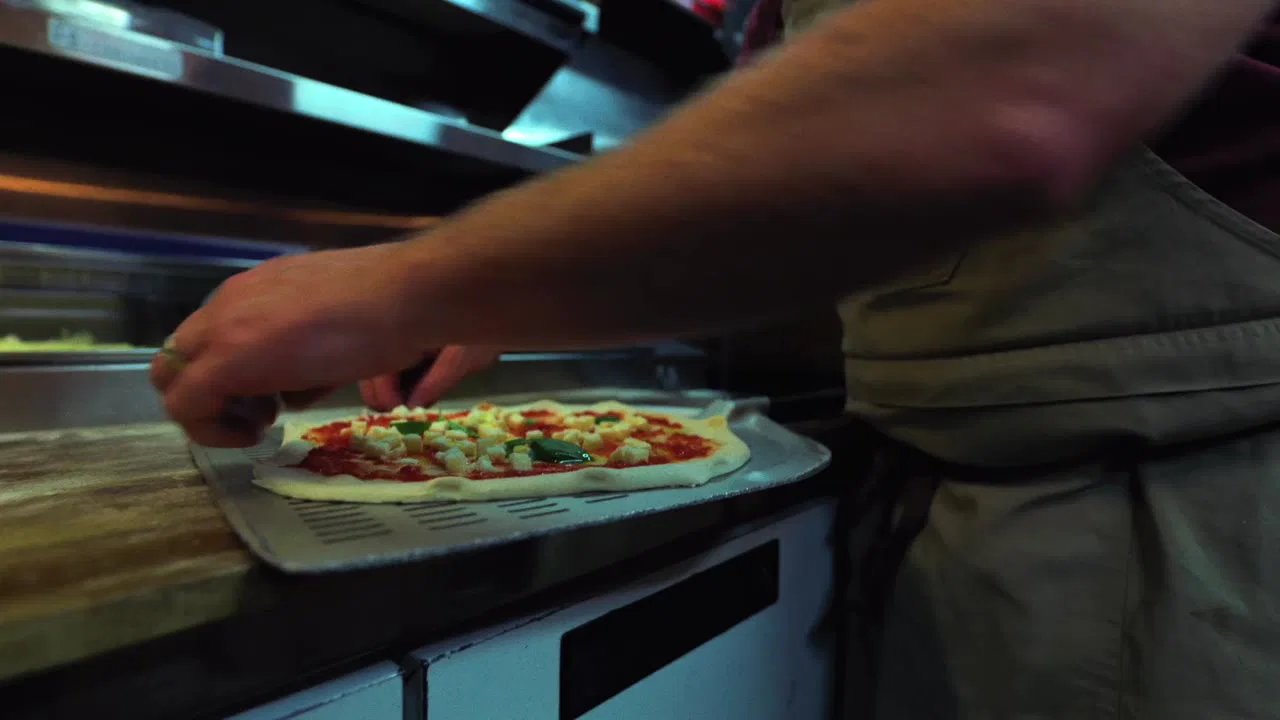 A Primo Pizza chef dressing a pizza on the peel next to the oven, filmed up close by Urban Media