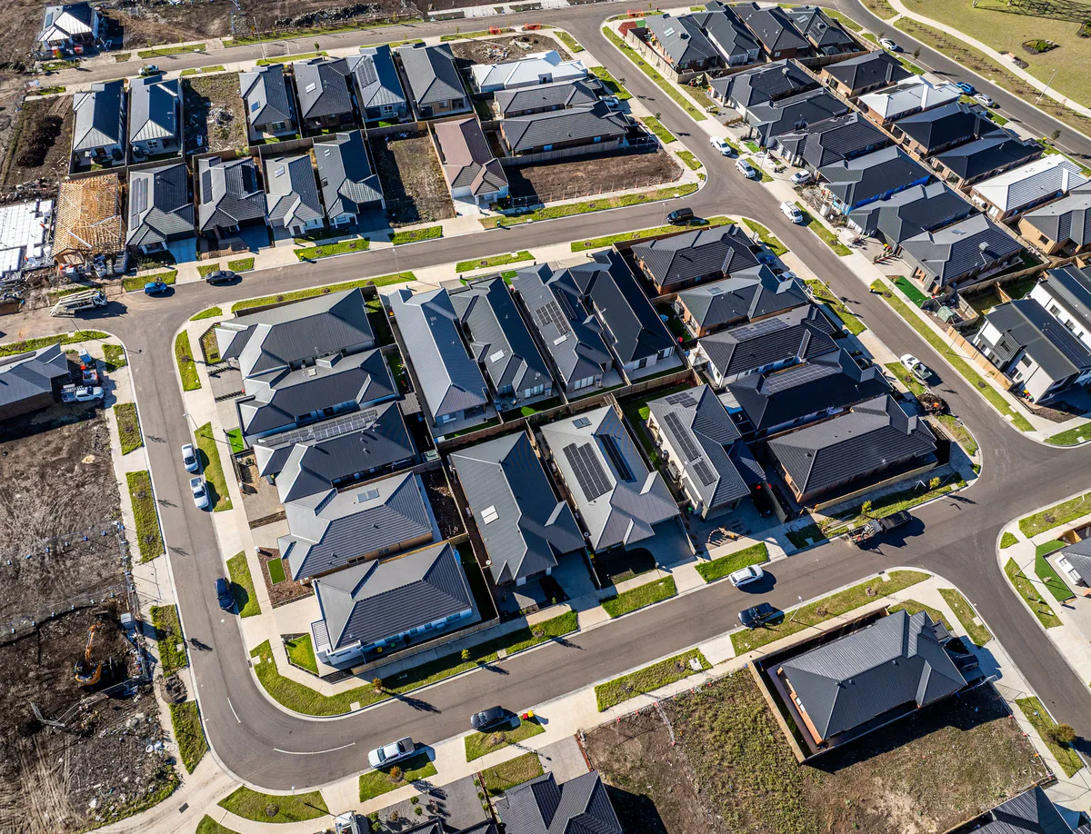 Drone view over a new housing estate, rows of dark roofs along curving streets