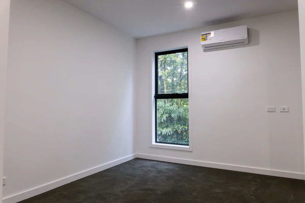 Empty bedroom with a black-framed window and a split-system unit