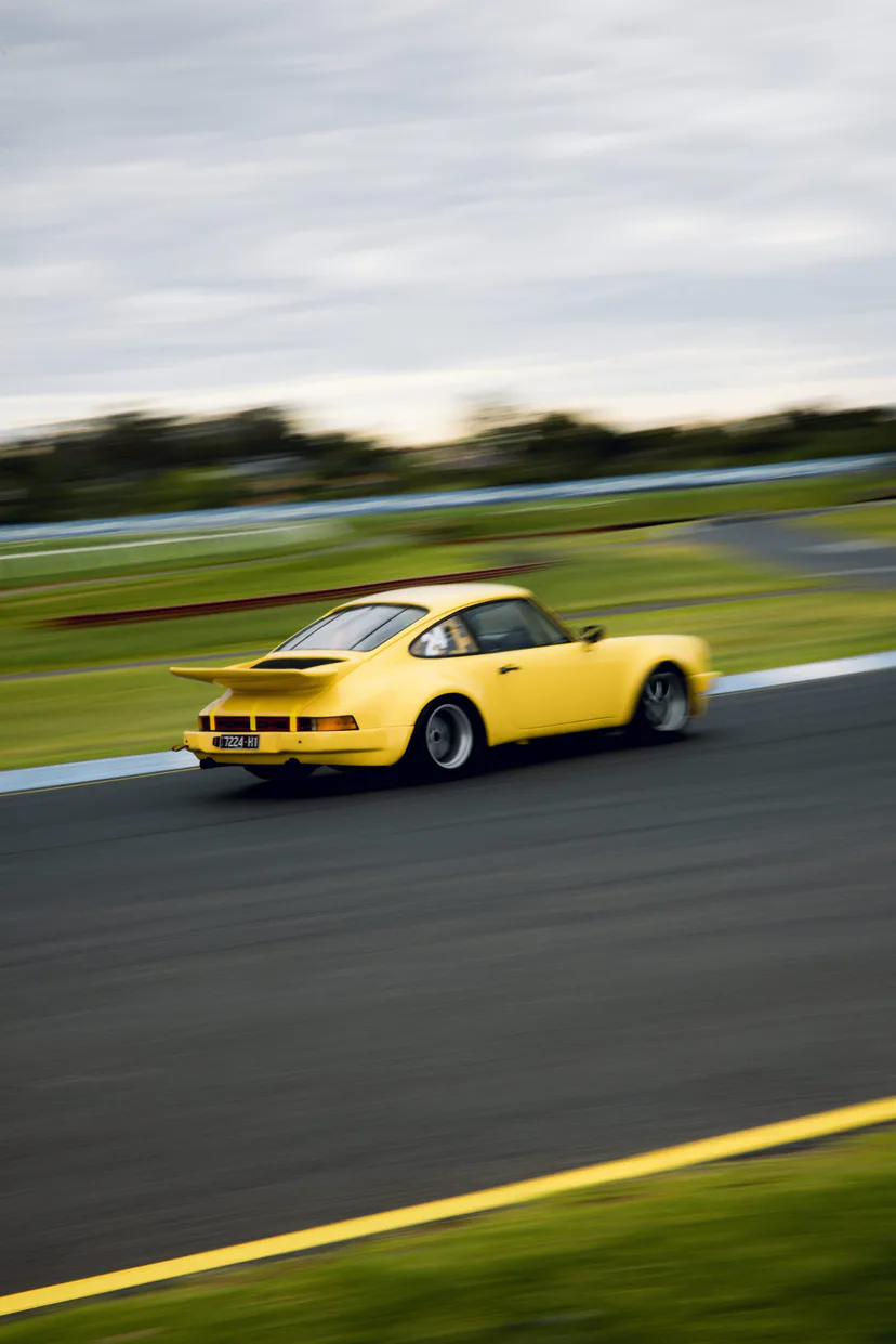 A yellow classic Porsche 911 panned at speed through a corner