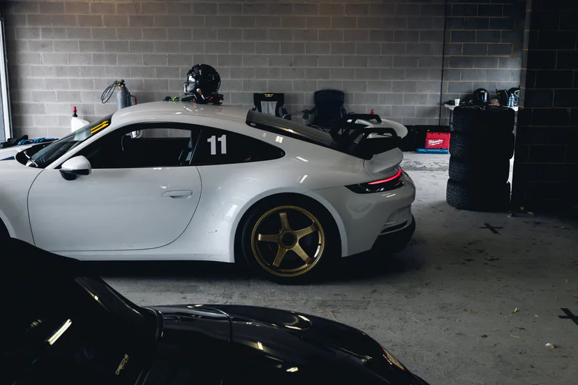 A white Porsche 911 GT3 in a pit garage, helmet resting on the roof