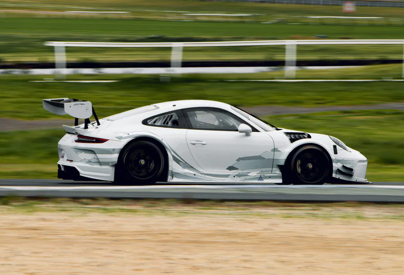 A white Porsche 911 GT3 Cup car with a rear wing, panned at speed past the fence