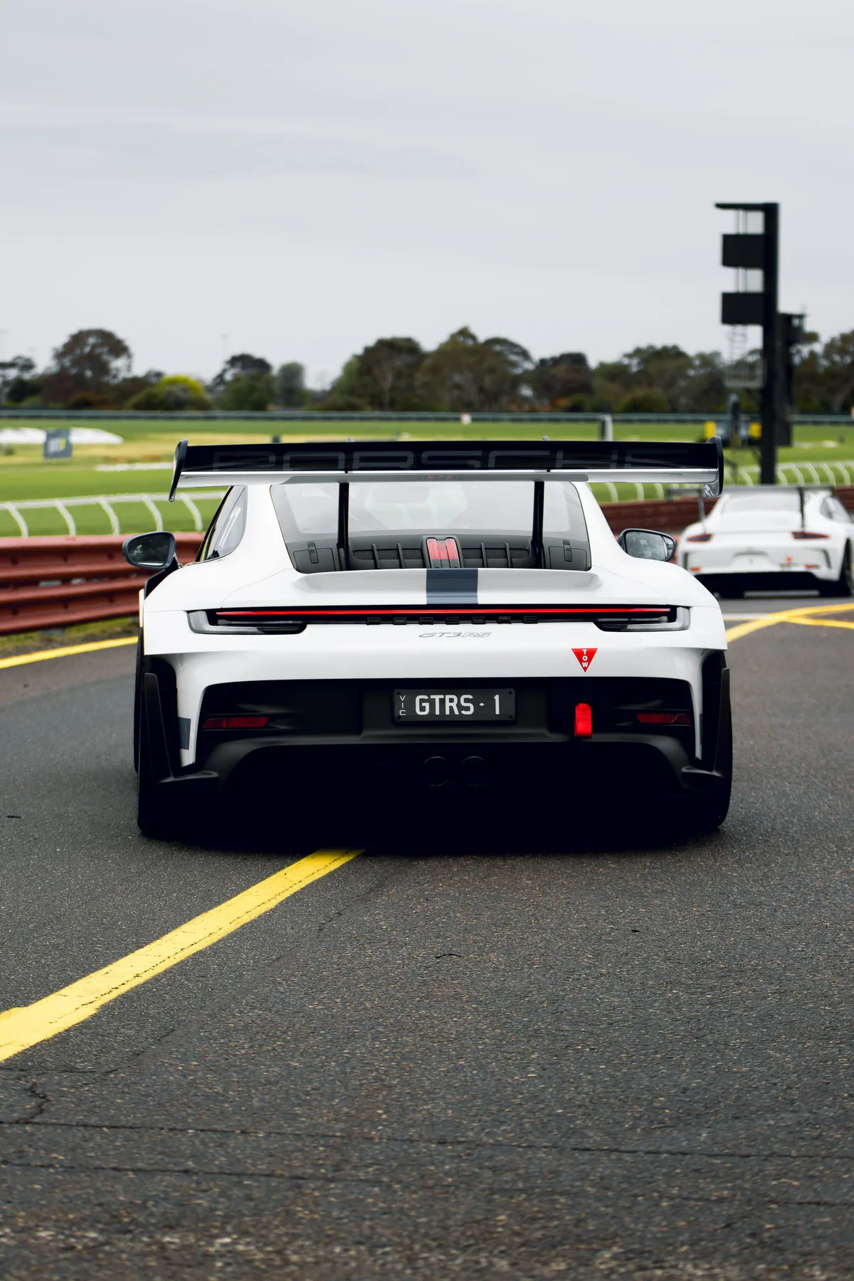 A white Porsche GT car from behind in pit lane, its wing up.