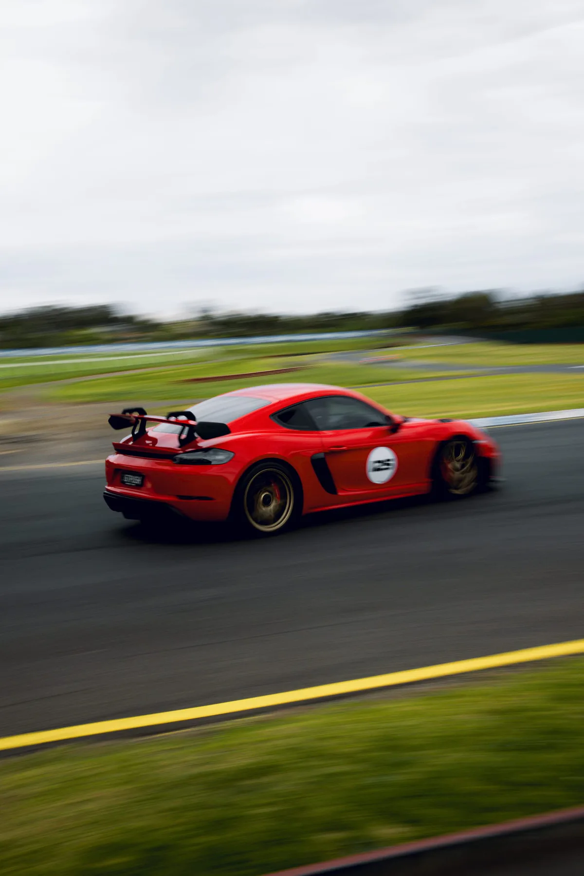 A red Porsche at speed past the grass.