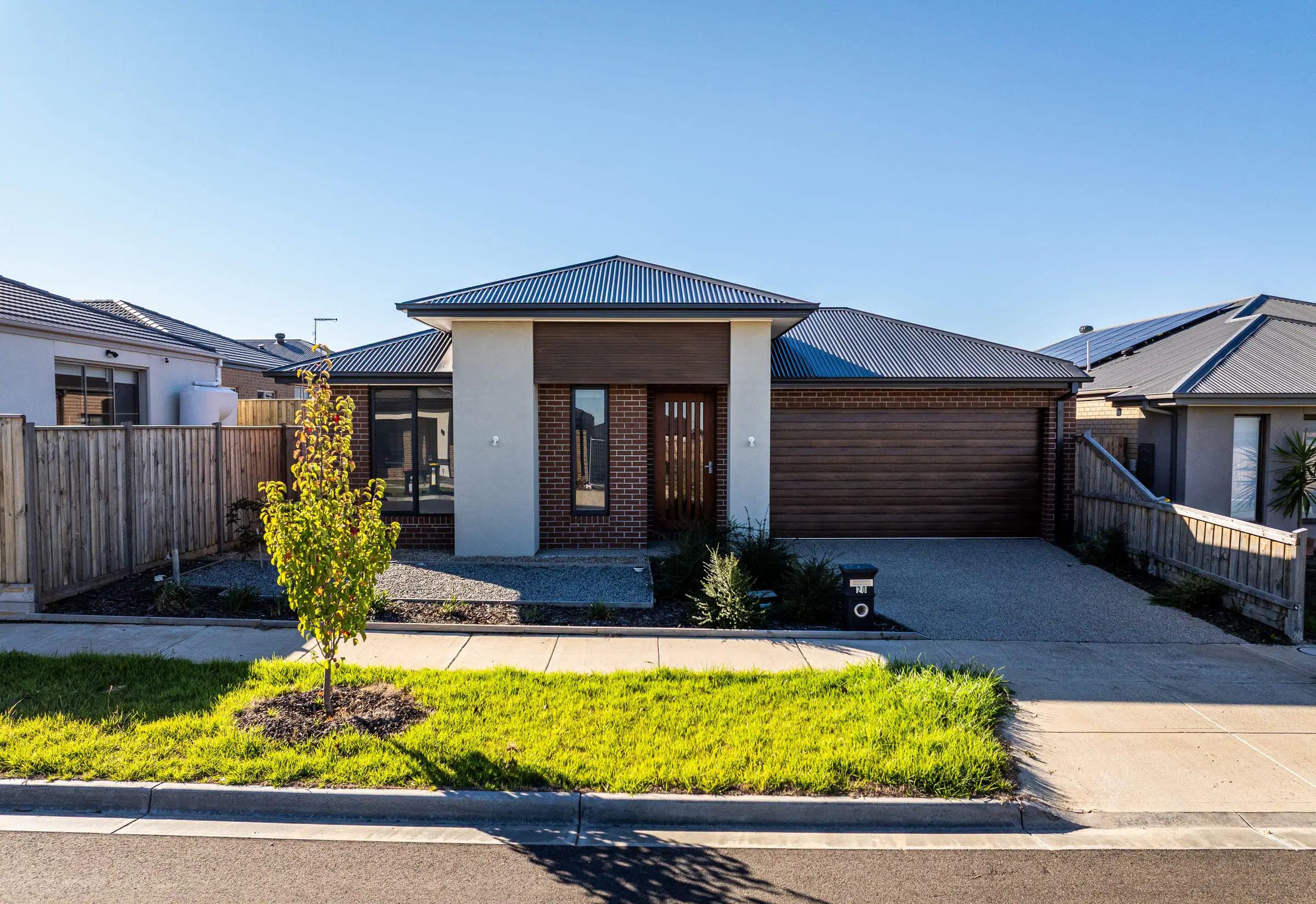 Front of a new single-storey home with a young tree and a fresh lawn