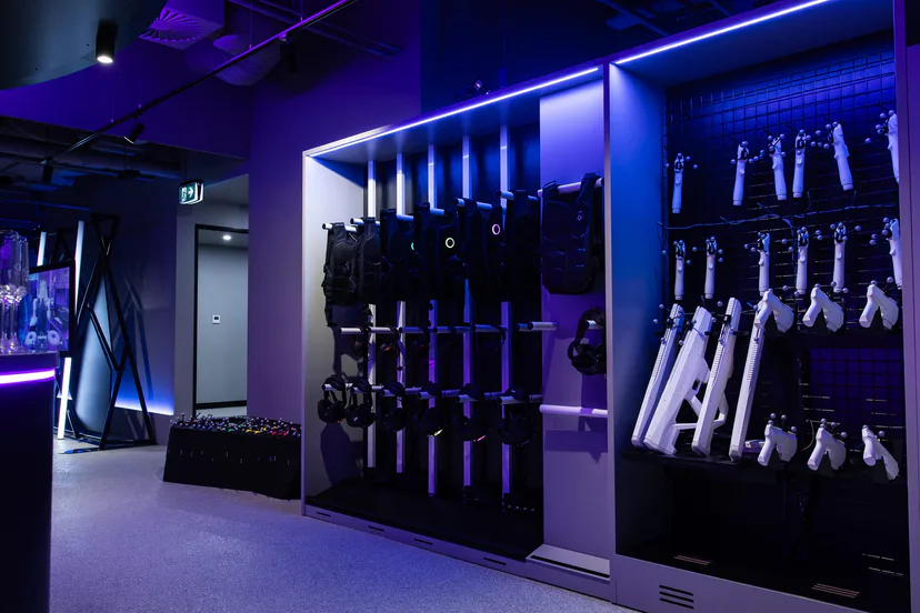 Haptic vests and blasters racked on a wall under purple light