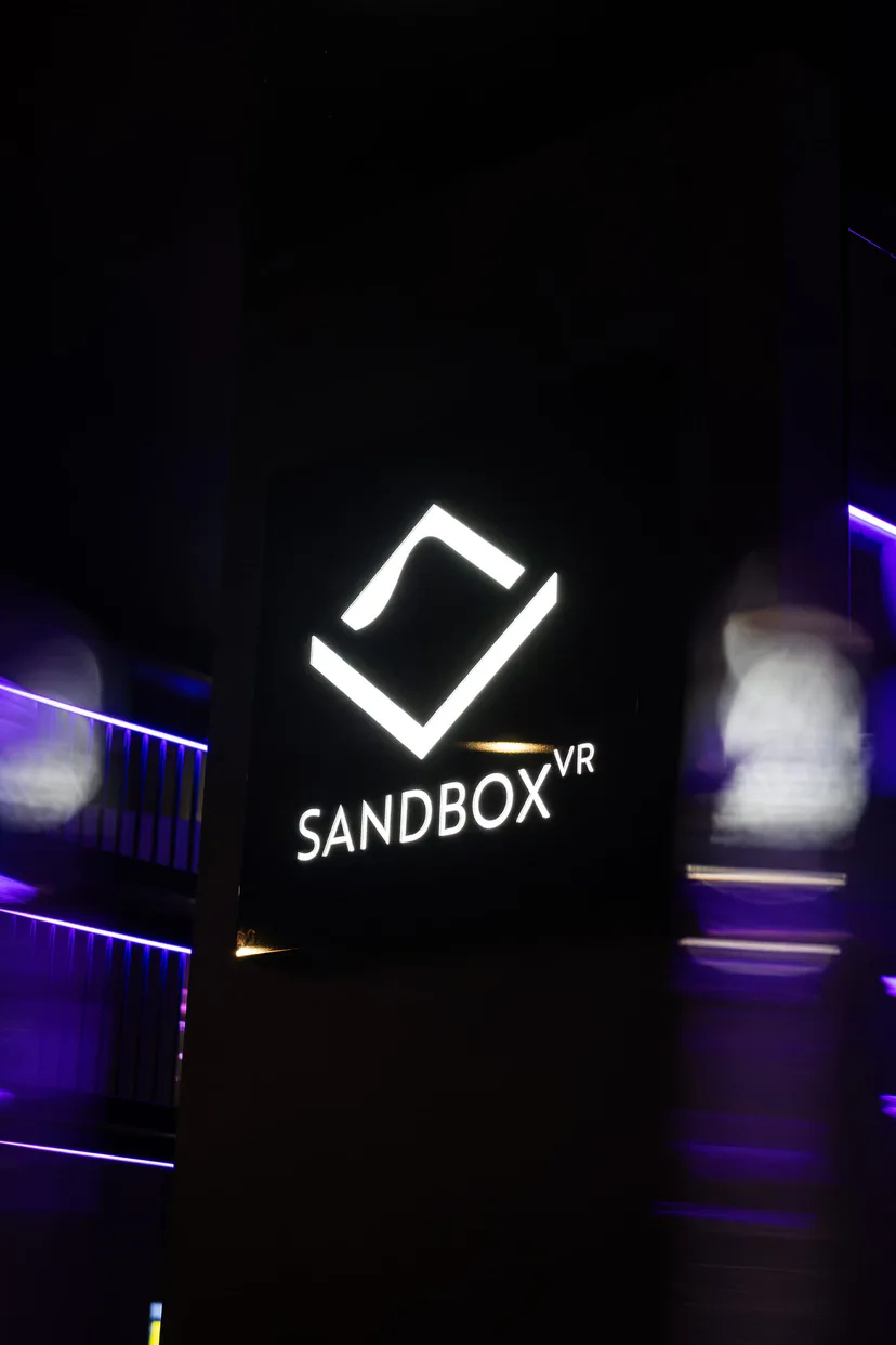 The illuminated Sandbox VR logo on a dark wall