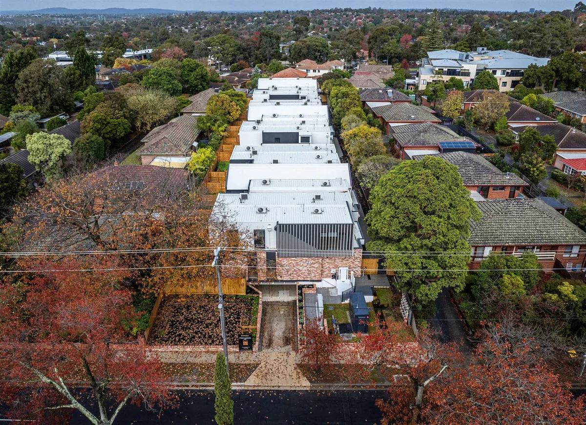 Drone view of a townhouse development among trees and neighbouring homes