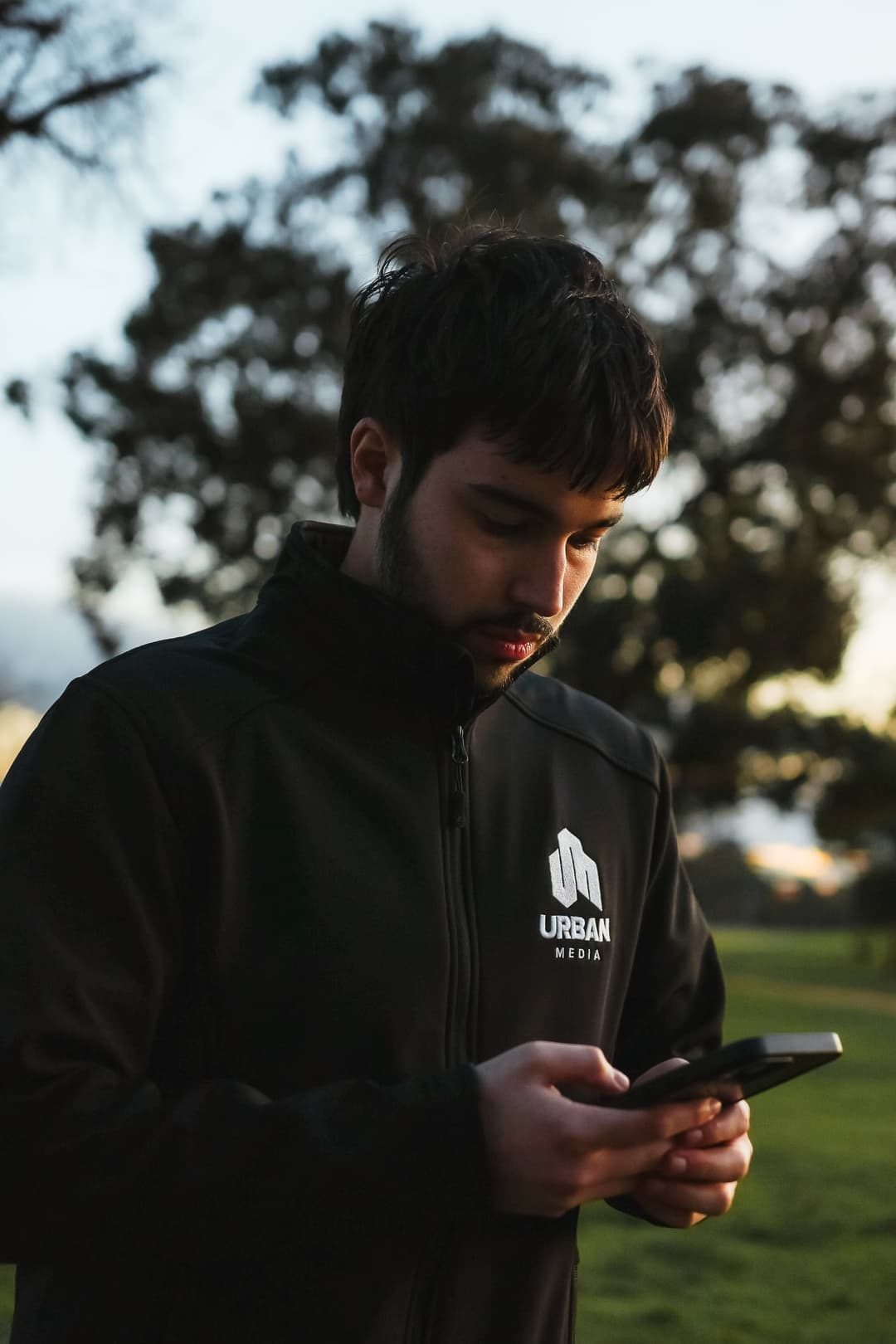 Gabe checking his phone in a park at golden hour