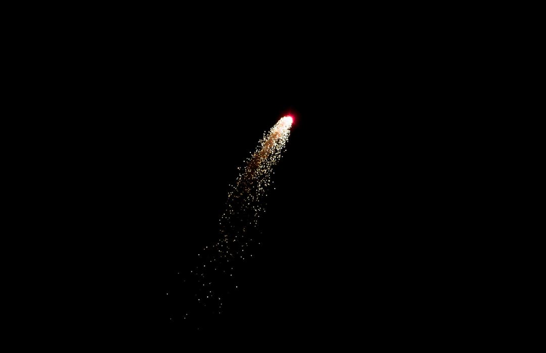 A firework shell trailing gold sparks as it climbs the night sky