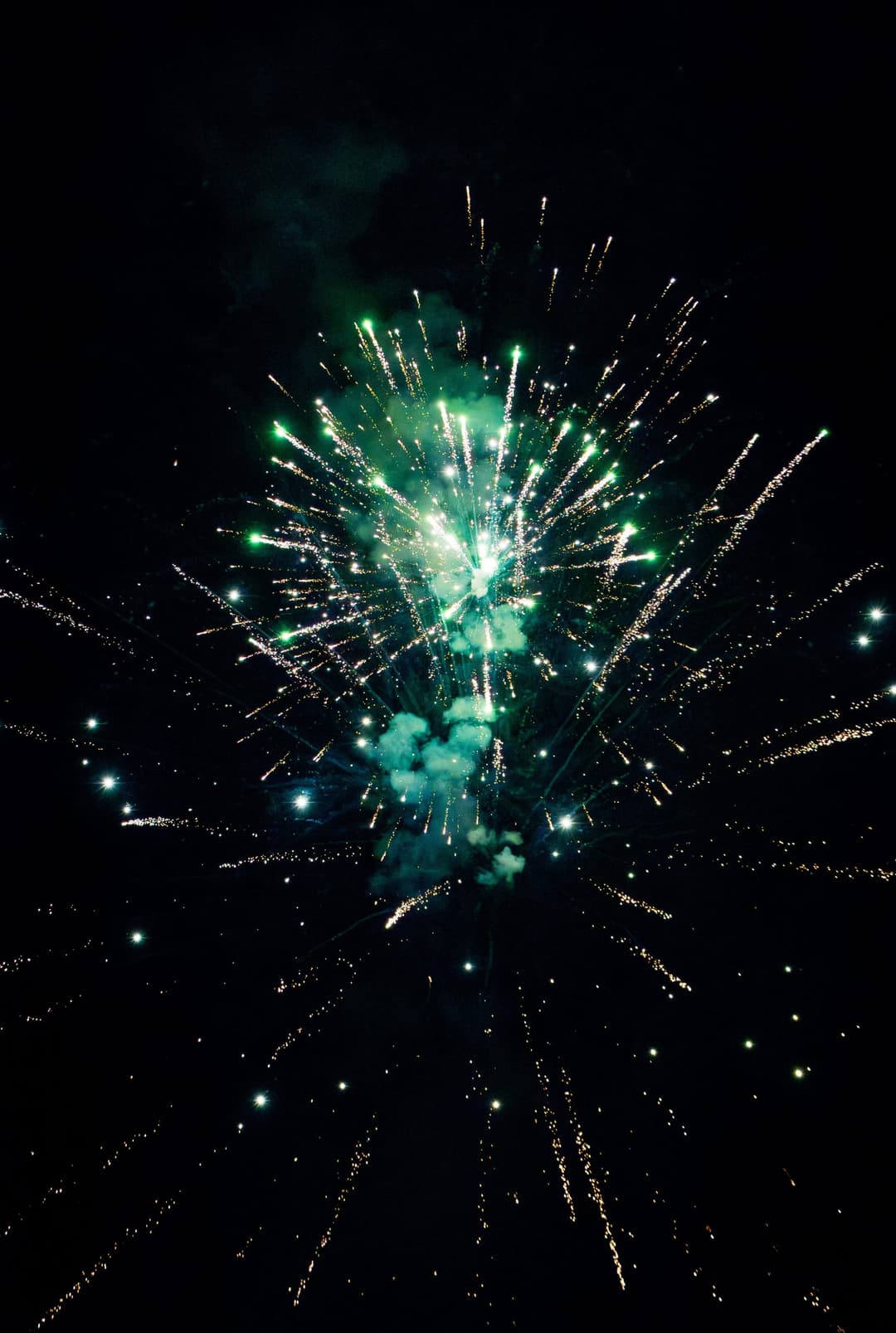 A green and gold firework burst with smoke trailing beneath it