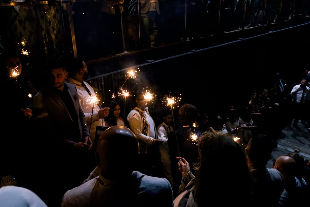 Guests holding sparklers in a dark venue during an evening event