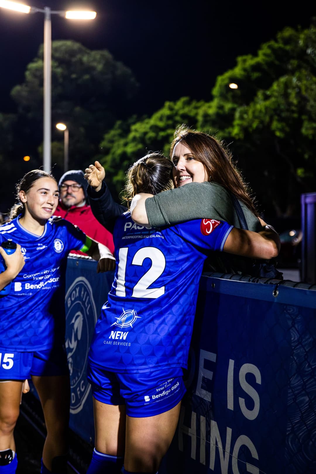 A Box Hill United player hugging a supporter over the fence after a night match