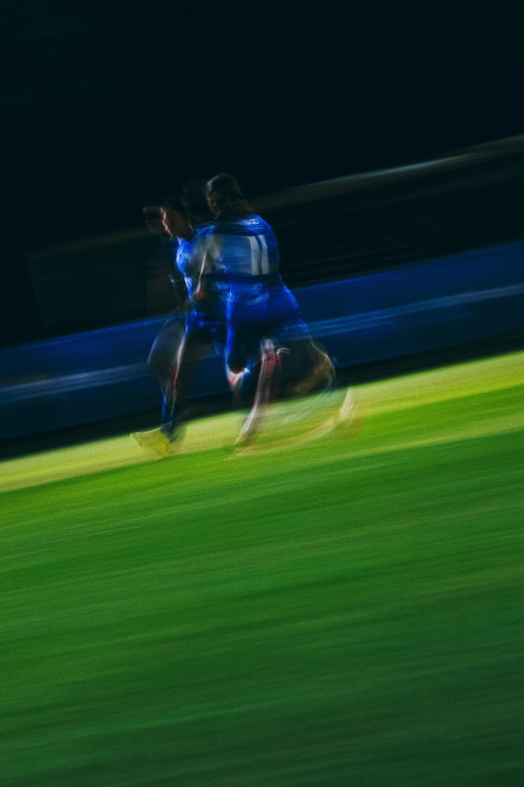 A Box Hill United player running the touchline under lights, motion blurred