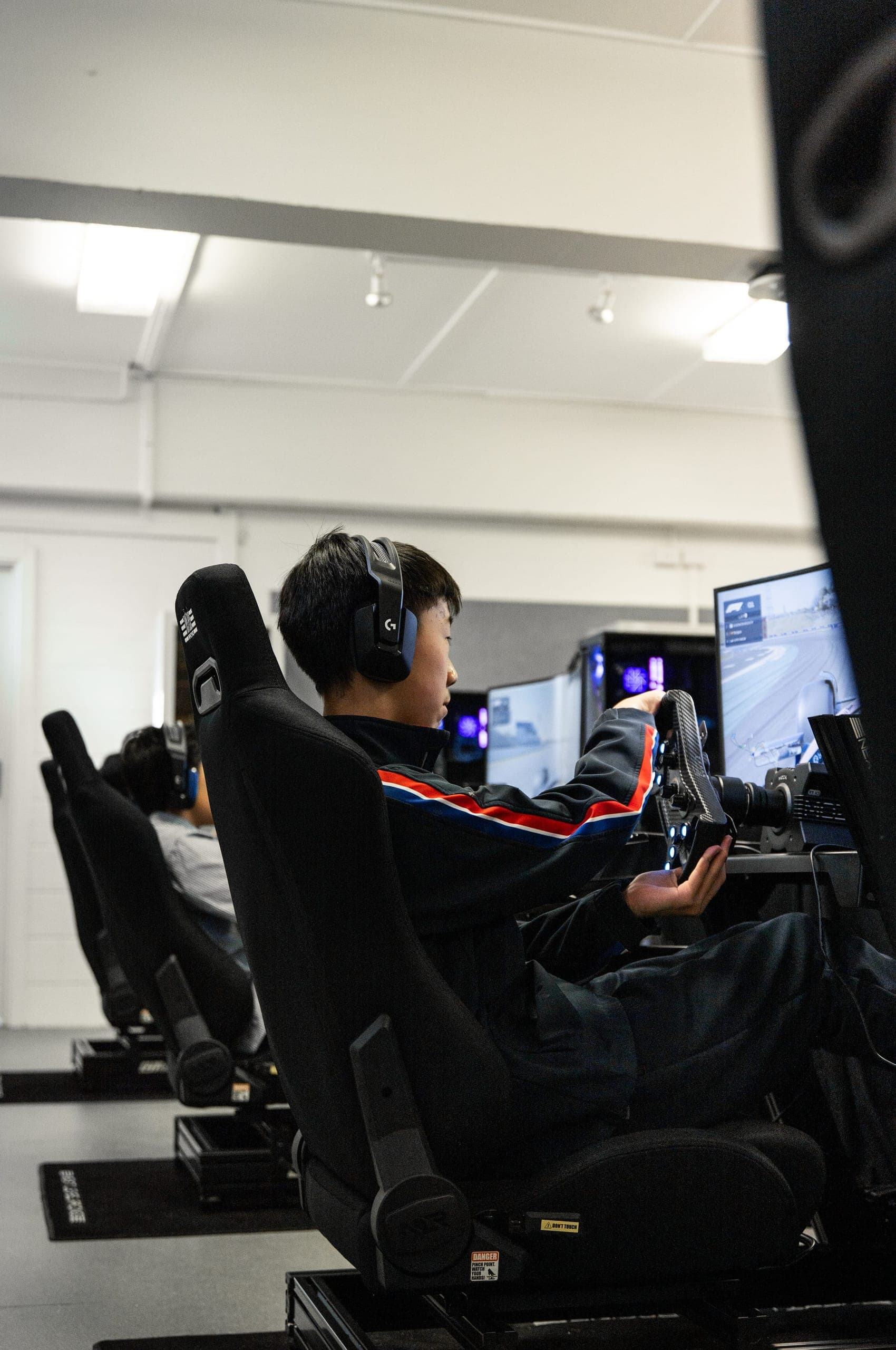 A student in a team jacket at a racing simulator, a row of rigs behind