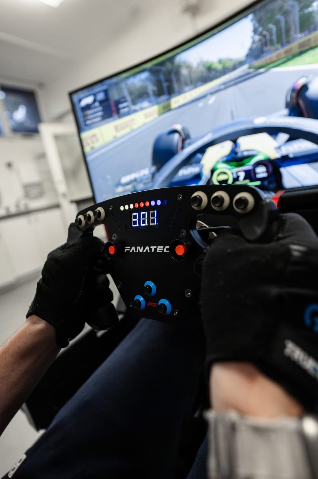 Gloved hands on a racing simulator wheel, a Formula 1 race on the screen ahead