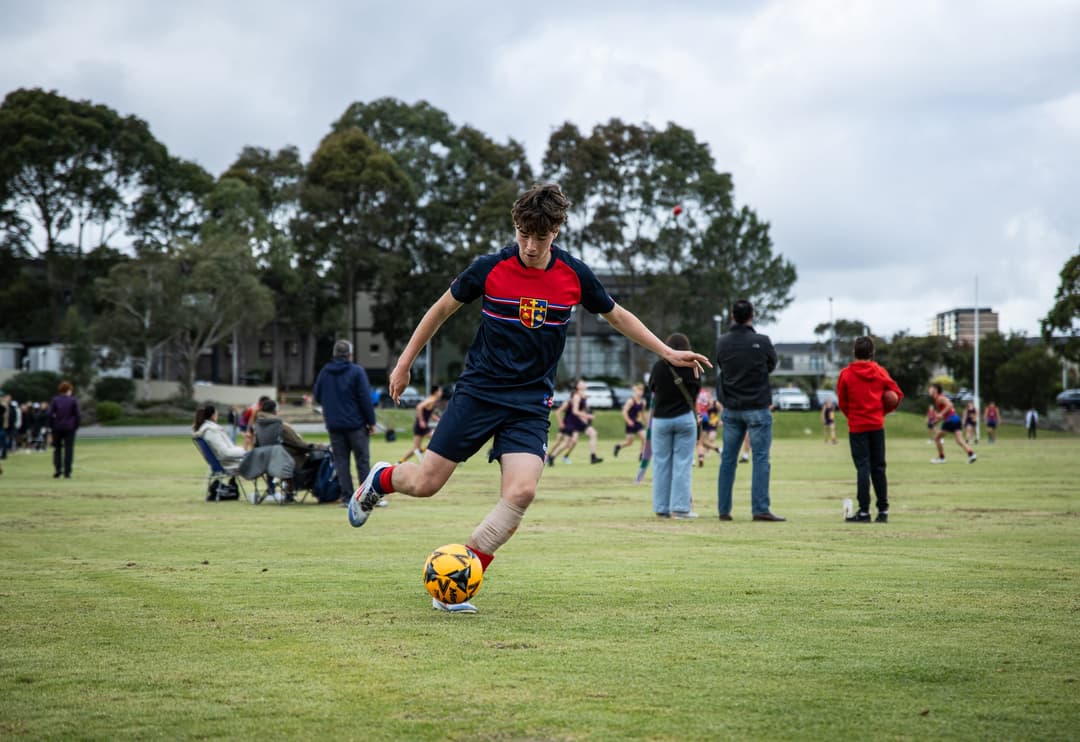 A Brighton Grammar student in the school's navy and red kit striking the ball