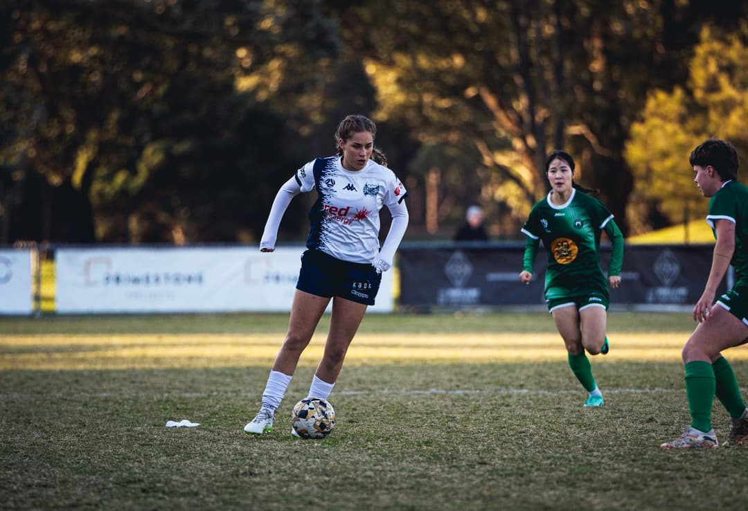 A Calder United player carrying the ball forward against two opponents