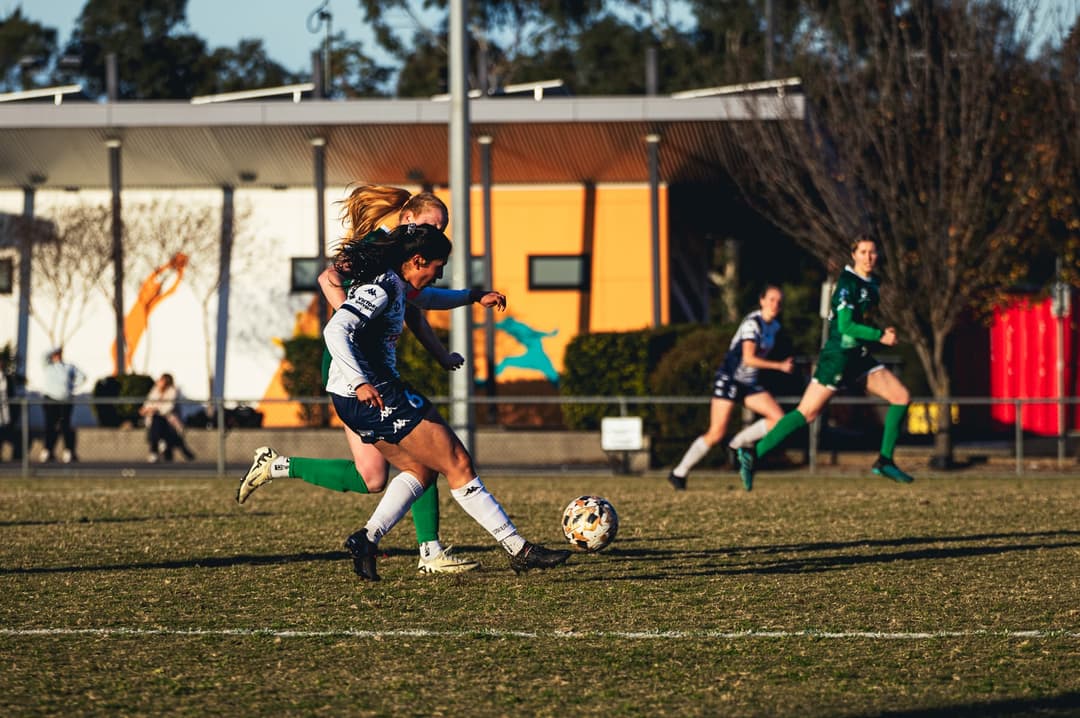 A Calder United player shielding the ball from an opponent at speed
