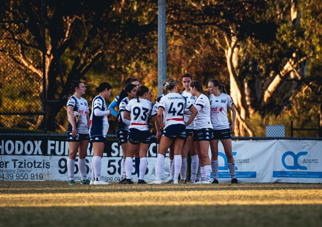 Calder United players gathered by the boundary fence at golden hour. Frame 8 of 12. Open it