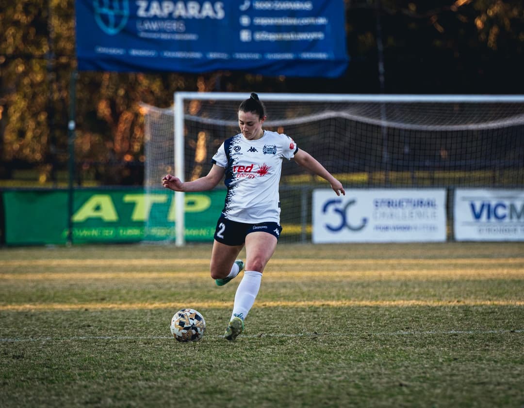 A Calder United player striking a long ball in front of the goal. Frame 7 of 12. Open it