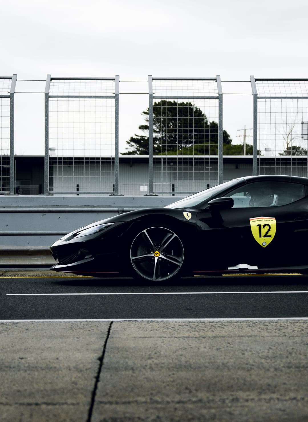 A black Ferrari carrying a number 12 rally plate on pit lane. Frame 1 of 6. Open it
