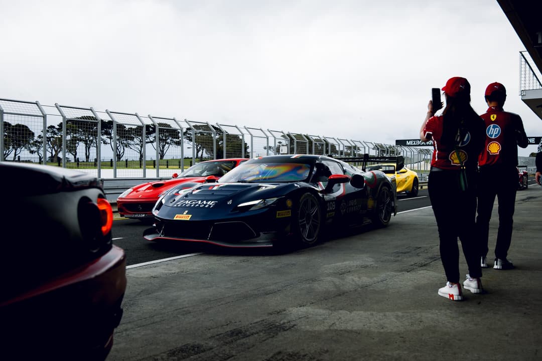 Ferraris queued in pit lane while two people in team gear photograph them
