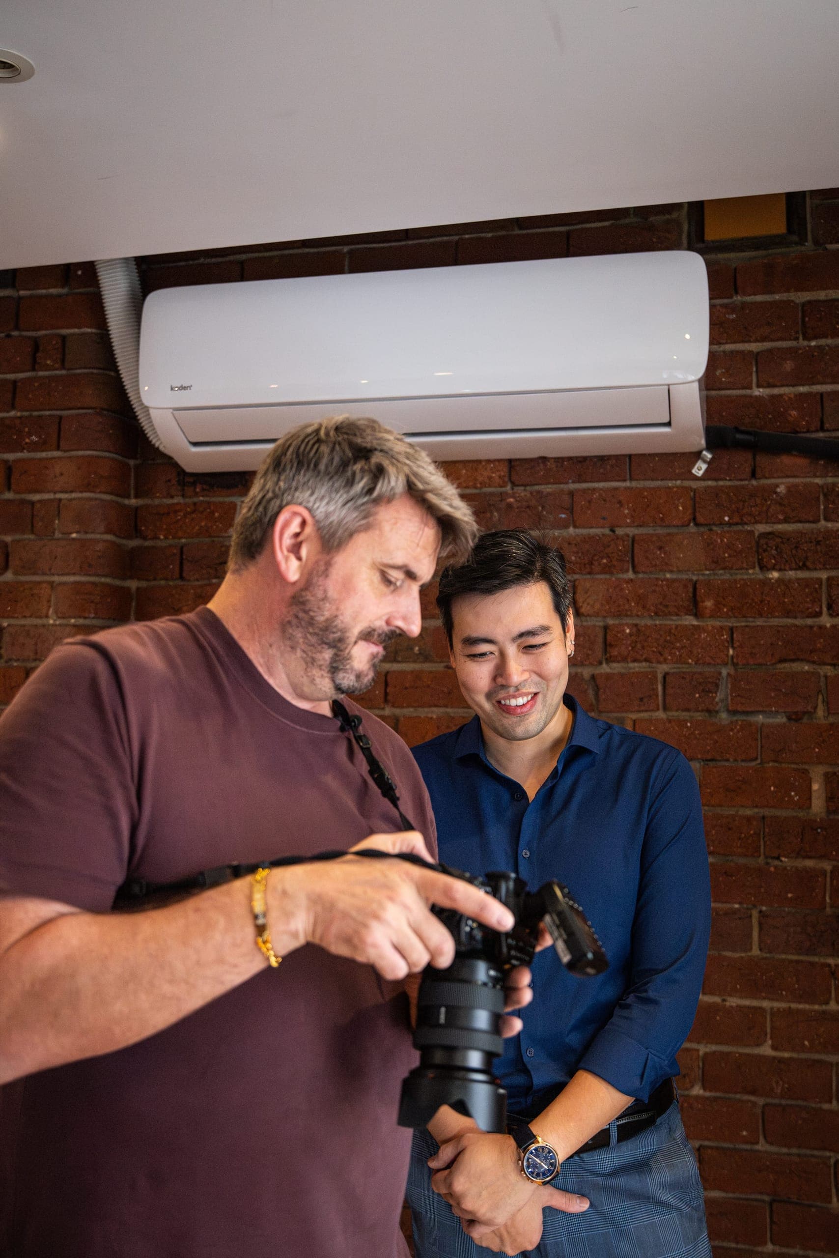 A photographer showing a client the back of the camera against a brick wall