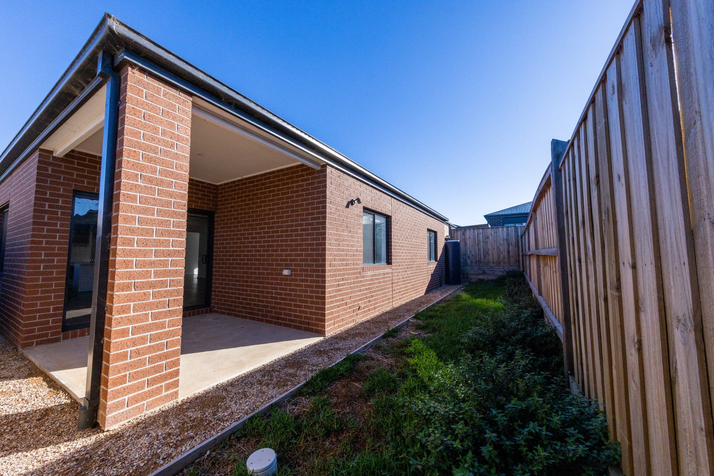 The side of a new brick home, covered alfresco and a paling fence down the side