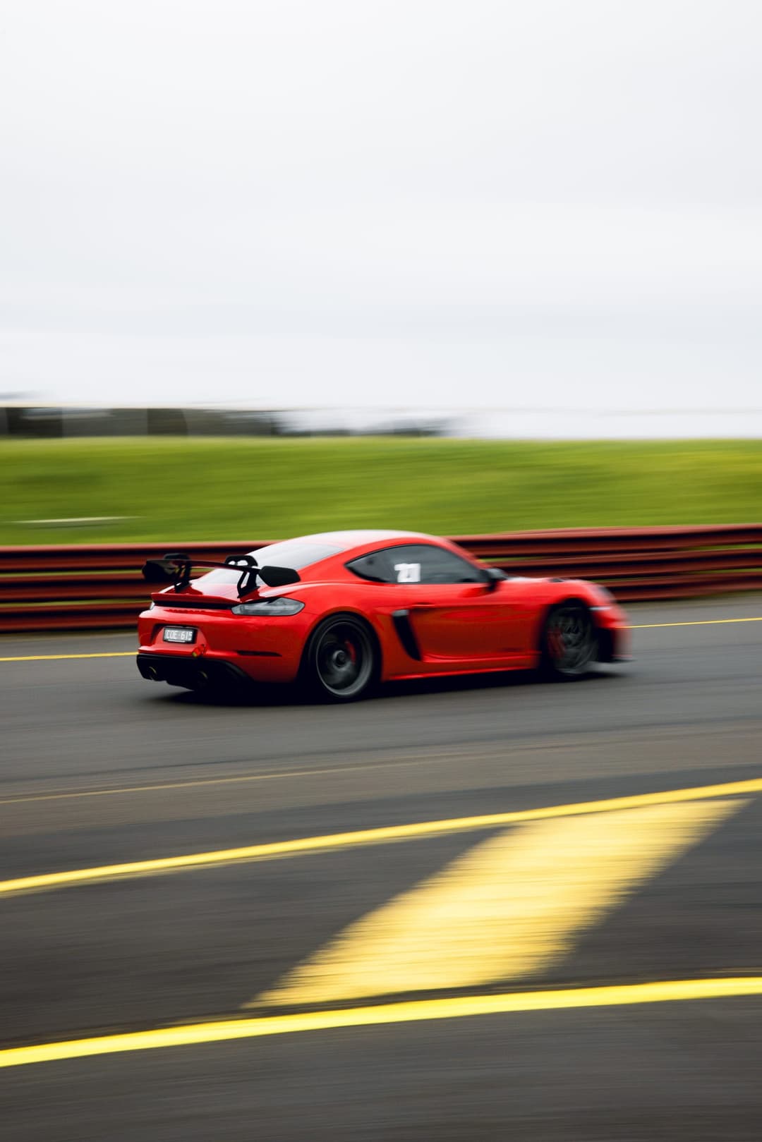 A red Porsche Cayman with a rear wing, panned at speed past the barrier