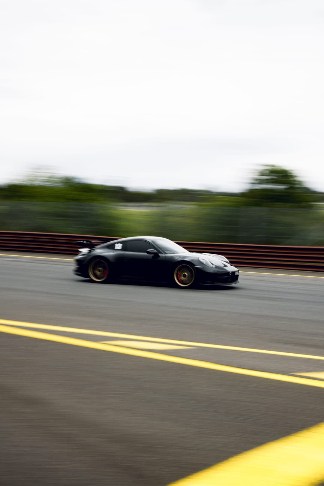 A black Porsche 911 on gold wheels, panned at speed on the circuit