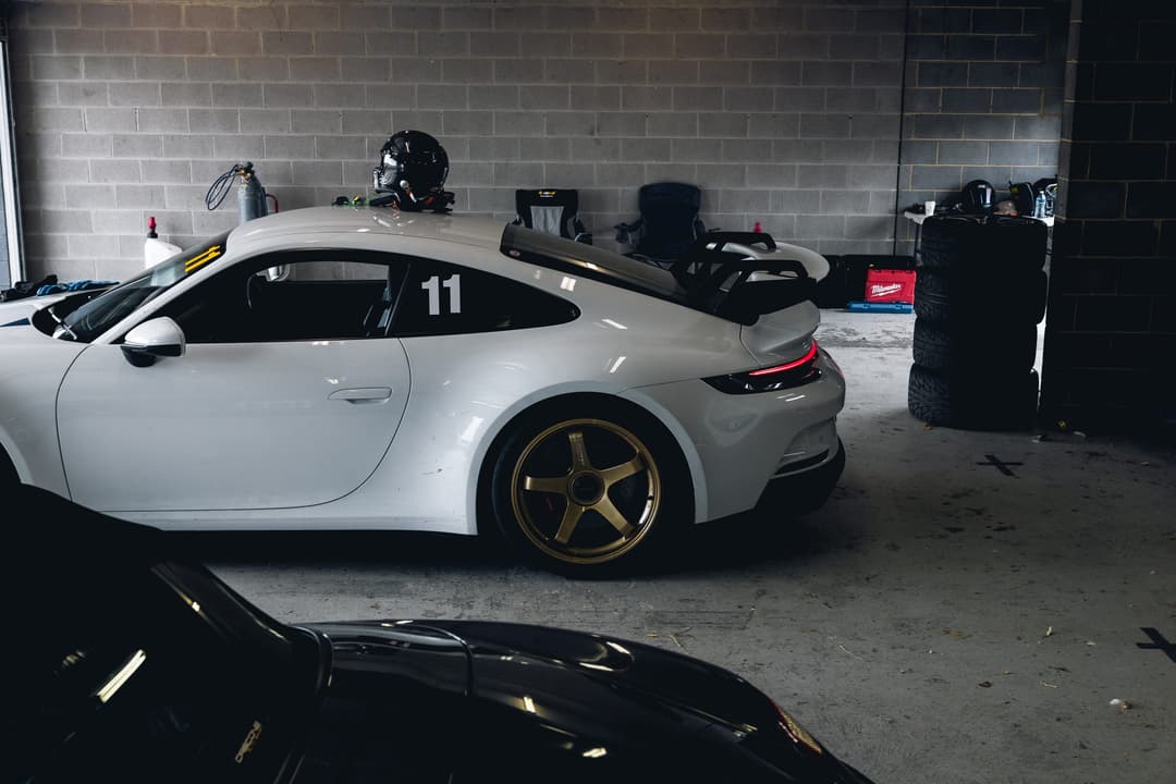 A white Porsche 911 GT3 in a pit garage, helmet resting on the roof