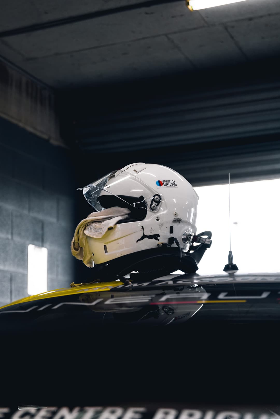 A racing helmet and gloves resting on a car roof in the pit garage. Frame 2 of 6. Open it