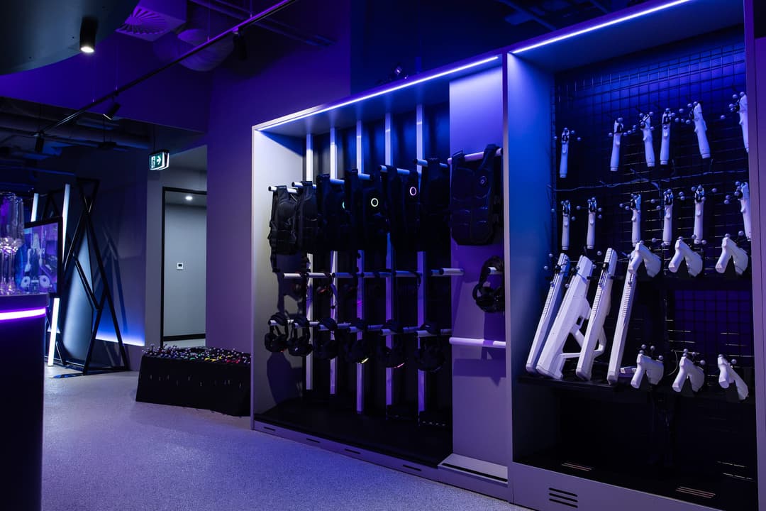 Haptic vests and blasters racked on a wall under purple light